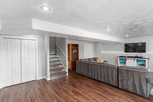 Unfurnished living room with a textured ceiling, stairs, and dark wood-style flooring