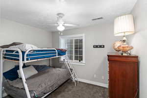 Bedroom featuring dark colored carpet, visible vents, a ceiling fan, a textured ceiling, and baseboards