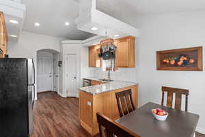 Kitchen featuring arched walkways, dark wood-style flooring, appliances with stainless steel finishes, a sink, and light stone countertops