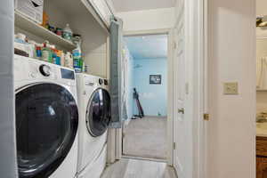 Laundry area featuring laundry area, light wood finished floors, light colored carpet, and washer and dryer