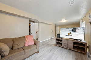 Living area with a textured ceiling, visible vents, baseboards, stairs, and light wood-type flooring