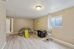 Game room featuring light wood-style flooring, baseboards, and a textured ceiling