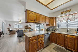 Kitchen with a peninsula, a sink, stainless steel dishwasher, a wealth of natural light, and brown cabinetry