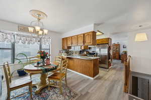 Kitchen with a peninsula, light countertops, appliances with stainless steel finishes, brown cabinetry, and decorative light fixtures