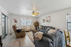 Living room with ceiling fan, light wood finished floors, visible vents, and baseboards