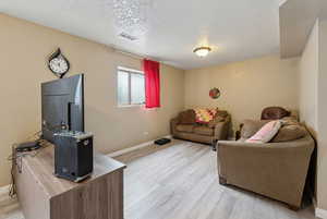 Living area with a textured ceiling, light wood finished floors, visible vents, and baseboards