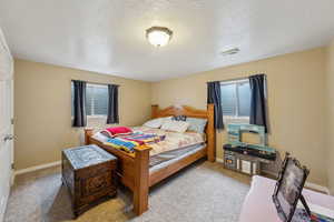 Bedroom with light carpet, visible vents, baseboards, and a textured ceiling