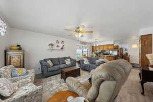 Living area featuring light wood-style flooring, baseboards, and ceiling fan with notable chandelier