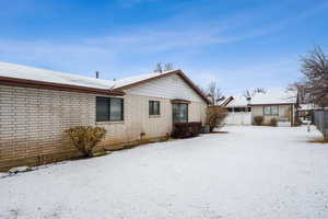 Snow covered rear of property featuring brick siding, central AC unit, and fence