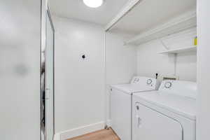 Washroom with laundry area, light wood-type flooring, washing machine and clothes dryer, and baseboards