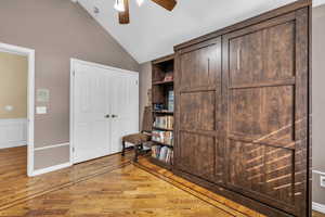 Unfurnished bedroom with a ceiling fan, wainscoting, vaulted ceiling, and wood finished floors