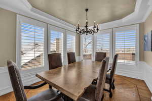 Dining room with a chandelier, wood finished floors, a wainscoted wall, and a raised ceiling