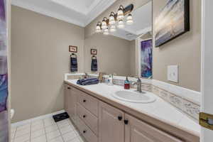 Bathroom featuring double vanity, baseboards, tile patterned floors, crown molding, and a sink