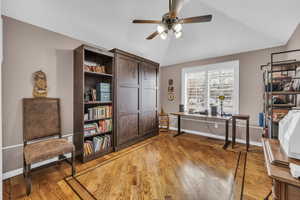 Office space featuring a ceiling fan, lofted ceiling, baseboards, and light wood finished floors