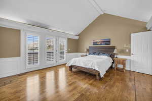 Bedroom featuring access to exterior, wainscoting, vaulted ceiling with beams, and wood finished floors