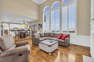 Living area with arched walkways, a wainscoted wall, crown molding, light wood finished floors, and a towering ceiling