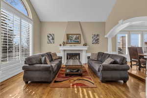 Living room with arched walkways, light wood finished floors, vaulted ceiling, and a fireplace