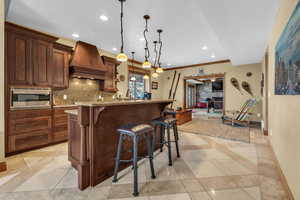 Kitchen with baseboards, custom exhaust hood, backsplash, stainless steel microwave, and pendant lighting