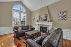 Living room with a wainscoted wall, vaulted ceiling, a fireplace, and light wood-style flooring