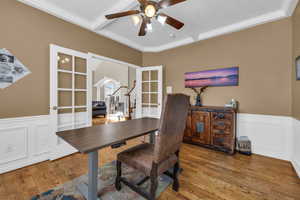 Office area with a wainscoted wall, crown molding, wood finished floors, and french doors