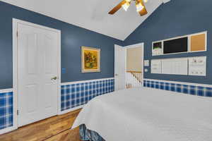 Bedroom with a wainscoted wall, a ceiling fan, vaulted ceiling, and wood finished floors