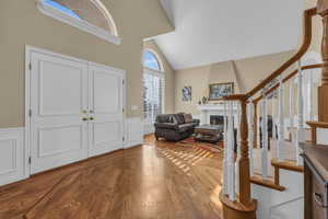 Entrance foyer featuring a large fireplace, visible vents, a wainscoted wall, stairway, and wood finished floors