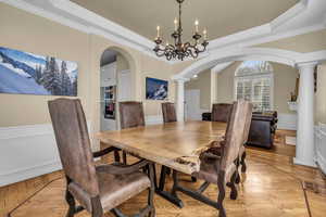 Dining room featuring decorative columns, arched walkways, a raised ceiling, a wainscoted wall, and light wood-type flooring