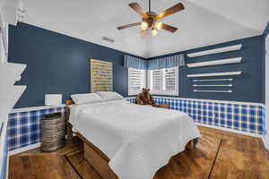 Bedroom with lofted ceiling, a wainscoted wall, visible vents, and wood finished floors