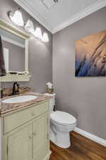 Half bathroom featuring toilet, wood finished floors, vanity, baseboards, and ornamental molding