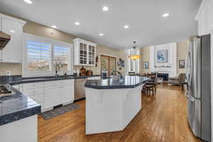 Kitchen featuring white cabinets, appliances with stainless steel finishes, dark countertops, a kitchen bar, and glass insert cabinets