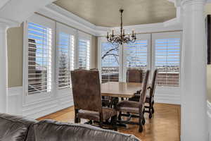 Dining area with decorative columns, light wood-style flooring, ornamental molding, a decorative wall, and a notable chandelier