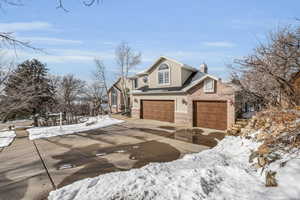 View of front of house with a garage, brick siding, driveway, stucco siding, and a chimney