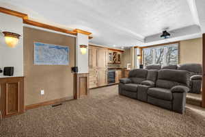 Cinema room featuring crown molding, a raised ceiling, light colored carpet, a textured ceiling, and beverage cooler