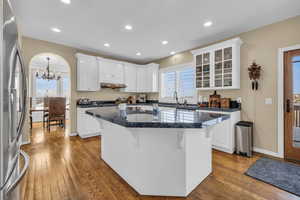 Kitchen with a kitchen island, white cabinetry, dark countertops, stainless steel fridge, and glass insert cabinets