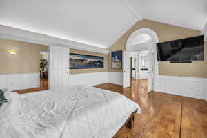 Bedroom with wainscoting, decorative columns, lofted ceiling with beams, and wood finished floors