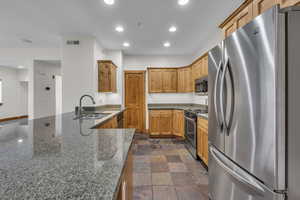 Kitchen with dark stone countertops, stone finish flooring, stainless steel appliances, a sink, and recessed lighting