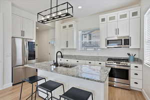 Kitchen with glass insert cabinets, appliances with stainless steel finishes, a kitchen island with sink, white cabinetry, and a sink