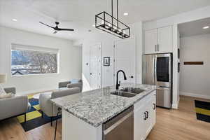 Kitchen featuring stainless steel appliances, hanging light fixtures, a kitchen island with sink, white cabinets, and a sink