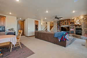 Living room with light carpet, baseboards, a textured ceiling, a stone fireplace, and recessed lighting