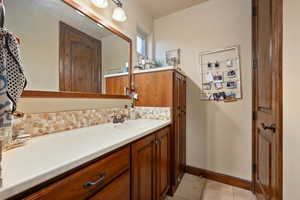 Bathroom featuring tile patterned flooring, baseboards, decorative backsplash, and vanity