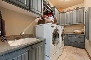 Clothes washing area with cabinet space, a sink, washer and clothes dryer, and stone tile floors