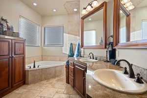 Full bathroom with stone tile flooring, double vanity, a sink, and a bath