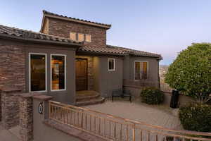 Back of property at dusk featuring stone siding, stucco siding, and a tiled roof