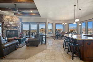 Living room with baseboards, a textured ceiling, stone tile flooring, a fireplace, and ceiling fan with notable chandelier