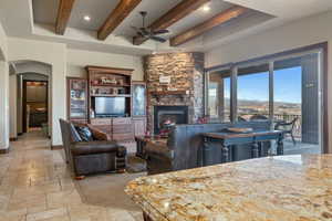 Living area featuring arched walkways, stone tile floors, a fireplace, baseboards, and beamed ceiling