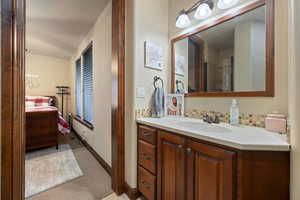 Ensuite bathroom with connected bathroom, baseboards, backsplash, and vanity