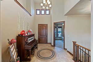 Foyer with baseboards, a high ceiling, a chandelier, and stone tile floors