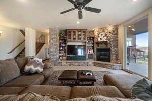 Living room with a ceiling fan, a stone fireplace, and stairs