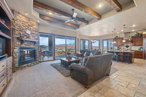 Living area featuring a fireplace, stone tile floors, recessed lighting, beamed ceiling, and ceiling fan with notable chandelier