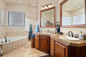 Full bathroom with double vanity, stone tile floors, a sink, and a bath